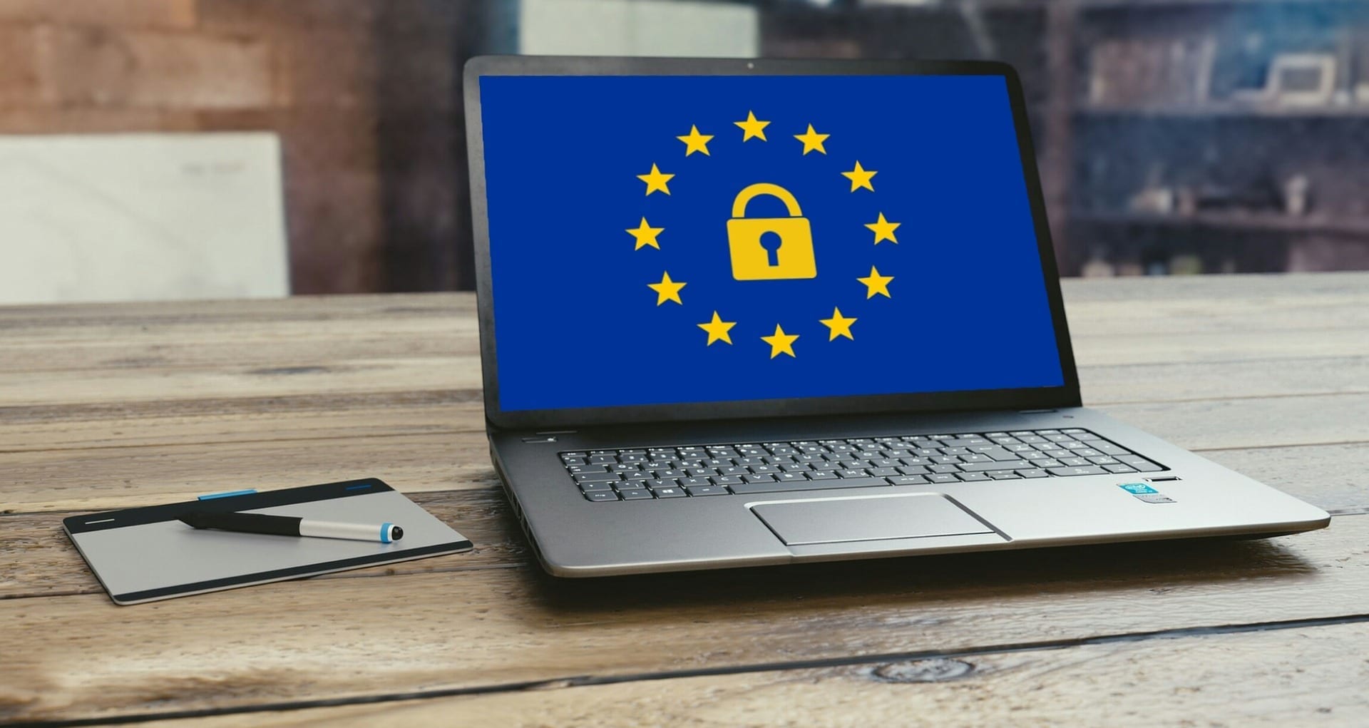 A laptop open on a table with the European flag displayed. In the centre of the flag is a gold padlock.