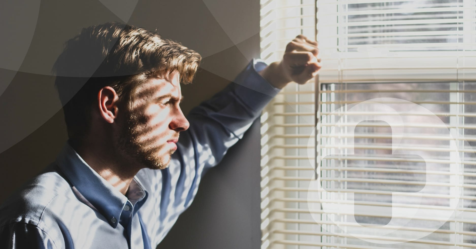 A man in a blue shirt looking out of a window whilst contemplating.