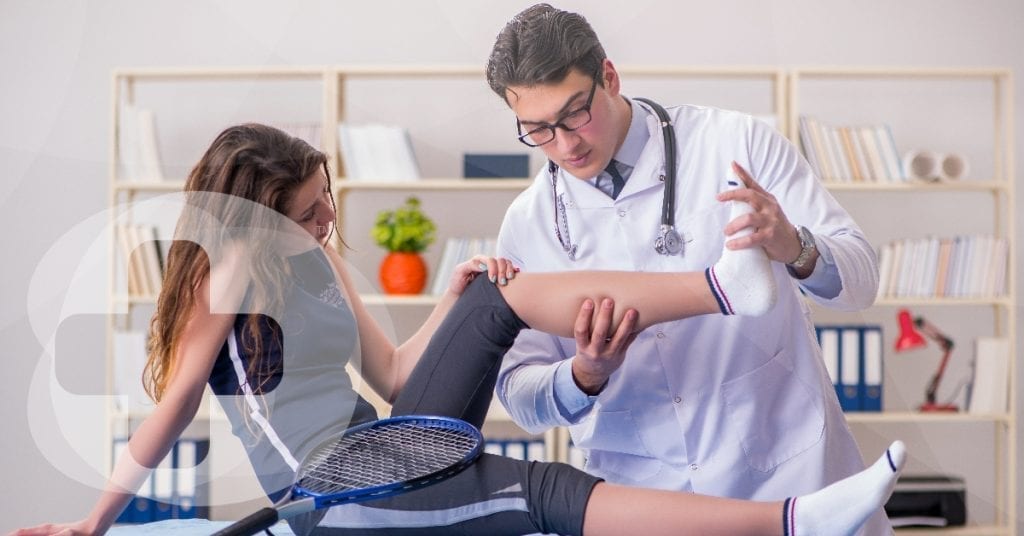 A doctor assessing a female tennis players leg with a skillbase first aid logo.