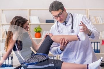 A doctor assessing a female tennis players leg with a skillbase first aid logo.