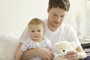 Man in white t-shirt holding a baby and a white teddy bear