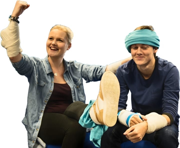 a lady and a man are sat after bandaging training. the lady has a bandage on her arm and leg whilst the man has a bandage on his head.