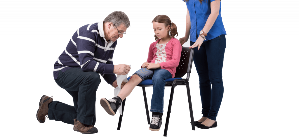 first aid at work course on site a small girl sits on a chair whilst a man bandages her right Knee. A woman is stood behind the chair overlooking the procedure.