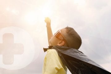 A small child with a cape made from a bin liner looking up at the sun.
