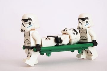 2 lego stormtroopers carrying another stormtrooper on a stretcher.