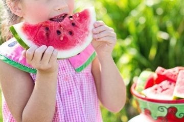 A young girl eating a slice of watermelon on a summers day.