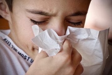 A young boy blowing his nose into a tissue.